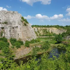 Malowniczy krajobraz rezerwat przyrody Kadzielnia z imponującą skałą, jeziorem i bujną zielenią pod błękitnym niebem.