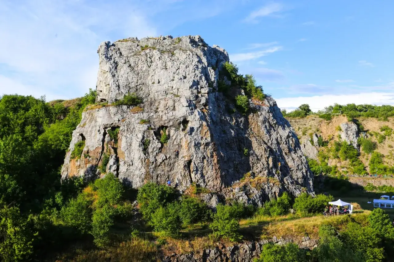 Wspinacze na skalnej ścianie w rezerwat przyrody Kadzielnia. W dole namioty i zielone drzewa.